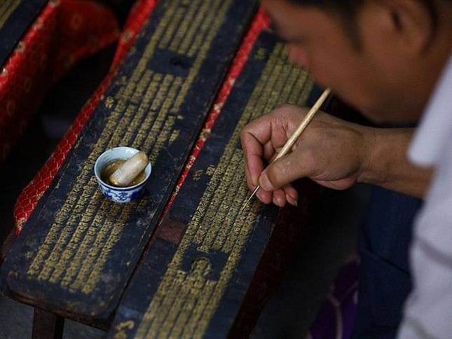 Artists in Nepal repaint Buddhist manuscript with gold as religious rituals halted for month